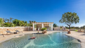 A clear swimming pool with lounge chairs, a pergola, and a stone wall. - 3666 Ca' Della Roccia by Perle di Puglia (Ostuni)
