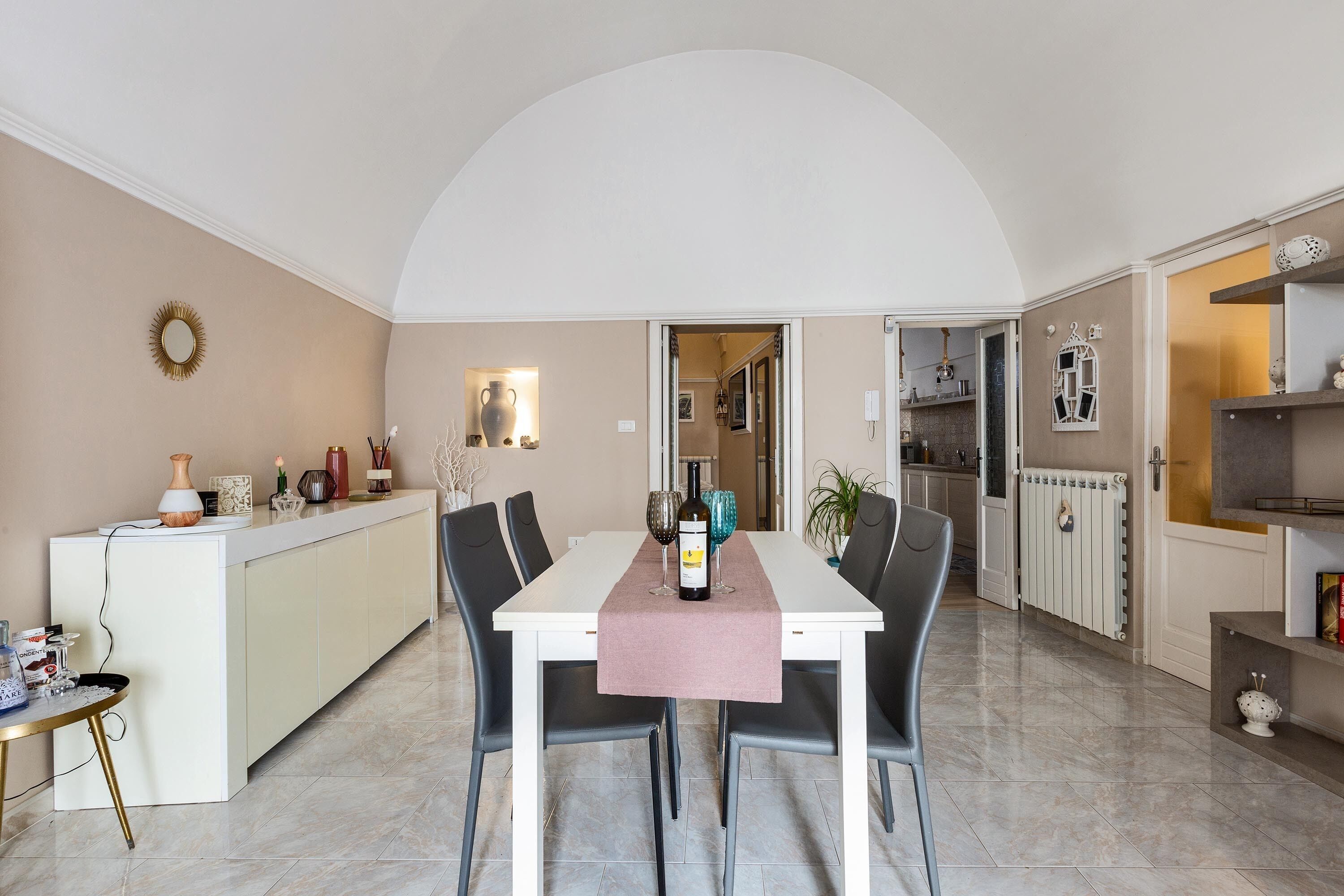 Un'area pranzo con un tavolo bianco, due sedie, un runner da tavolo rosa e una bottiglia di vino.
