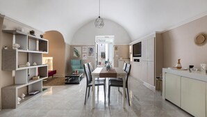 A spacious dining area with a high ceiling and a modern chandelier, leading to a kitchen area with a large island and built-in cabinets. - 3668 Appartamento Leonard by Barbarhouse (Carovigno)