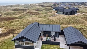 Ett modernt hus med en stor terrass och utsikt över de omgivande sanddynerna.