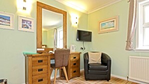 A room with a wooden desk, a chair, a television mounted on the wall, and a radiator. - Tingle Creek Hotel (Kyle)