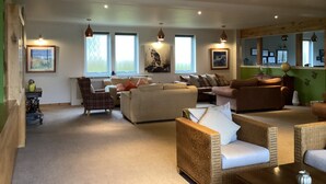 A spacious living room with multiple seating areas, large windows, and ceiling lights. - Tingle Creek Hotel (Kyle)