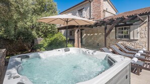 Un bain à remous doté d’une pergola et de chaises longues, entouré de murs en pierre et d’arbres.