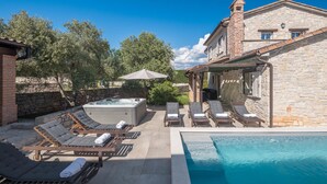 Un espace piscine avec des chaises longues, un jacuzzi et un bâtiment en pierre.
