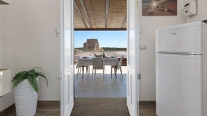 An open doorway leading to a patio with a table set for dining, a refrigerator, and a potted plant. - 3358 Terrazza Belvedere by Barbarhouse (Melendugno)