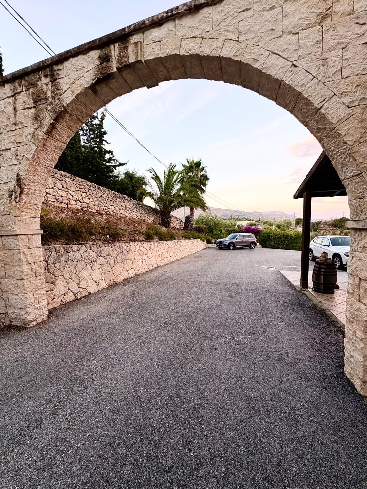 A stone archway leading to a paved road with parked cars and a building with a covered porch.