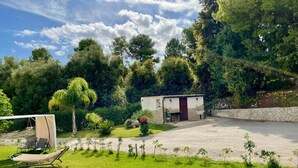 Une maison avec une allée pavée, un petit jardin agrémenté d’une chaise longue et un mur en pierre.
