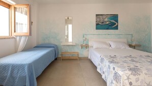 Une chambre avec deux lits, une fenêtre avec des rideaux, un tableau représentant un paysage côtier et une table de chevet avec une lampe.