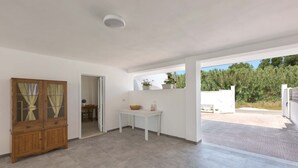 Une pièce spacieuse avec un meuble en bois, une petite table sur laquelle se trouve un panier, et une vue sur un jardin par une porte ouverte.