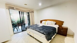 A bedroom with a bed, a nightstand, a sliding glass door to a balcony, and a tiled floor. - 6 Bedroom House @ Gungahlin Town Center (Gungahlin)