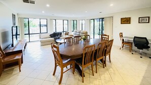 A spacious room with a large dining table surrounded by wooden chairs, a sofa, and a television. - 6 Bedroom House @ Gungahlin Town Center (Gungahlin)