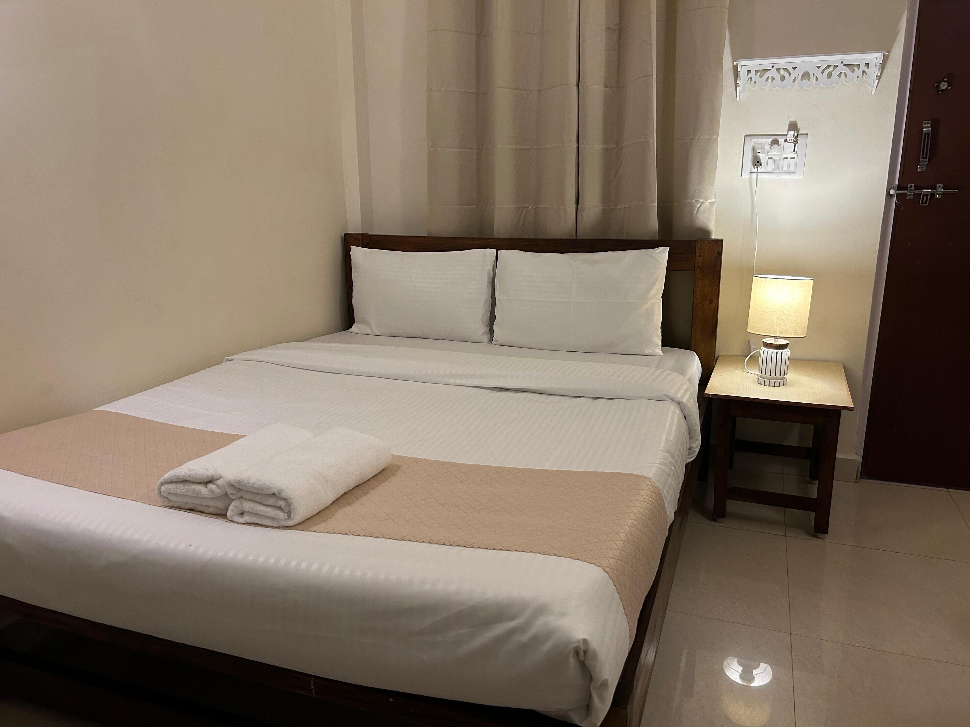 Un lit bien fait, avec une serviette pliée, une table de chevet avec une lampe et une porte avec un interrupteur.