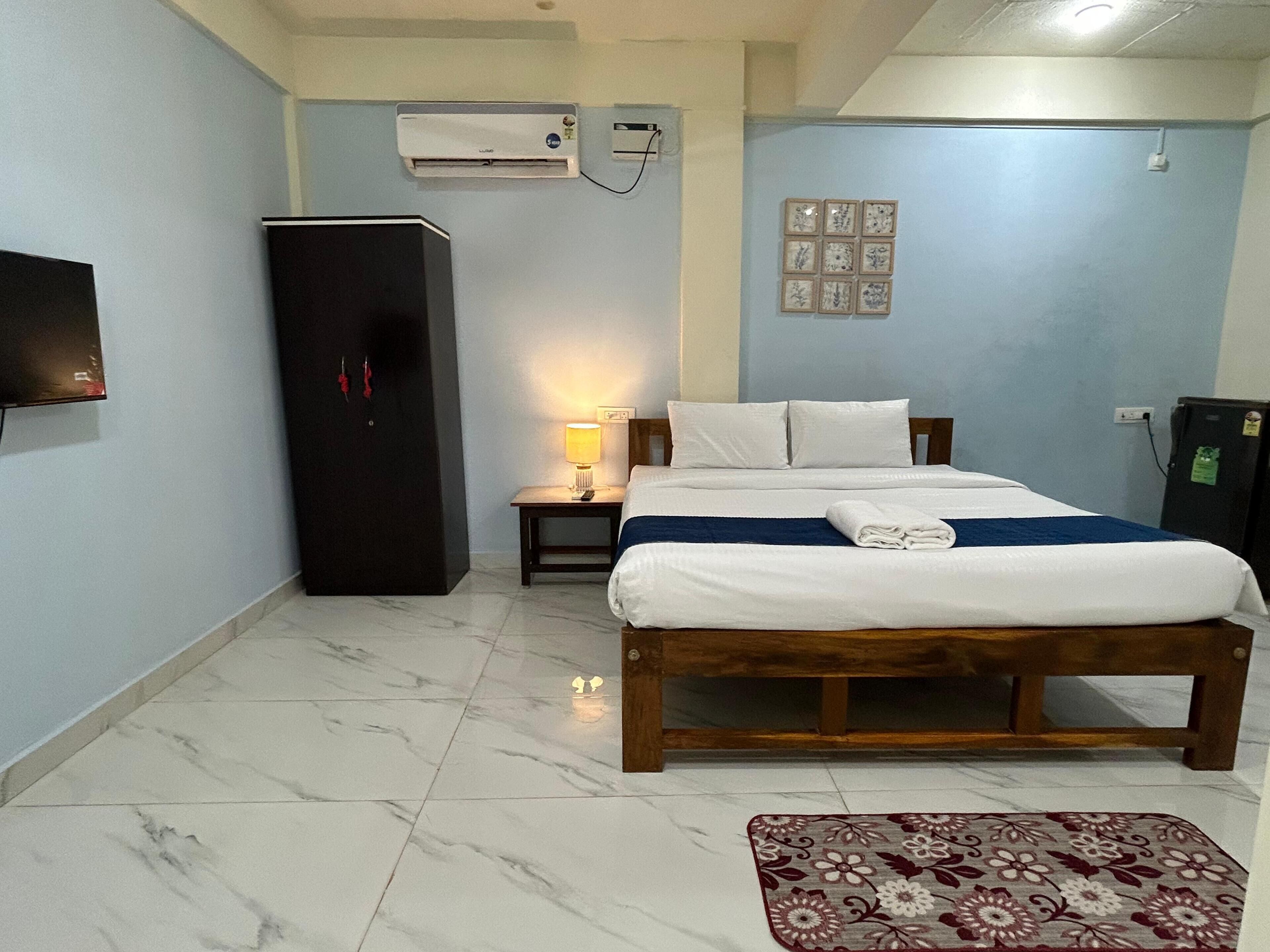Habitación de hotel con cama, mesita de noche, lámpara, aire acondicionado, televisor y armario.