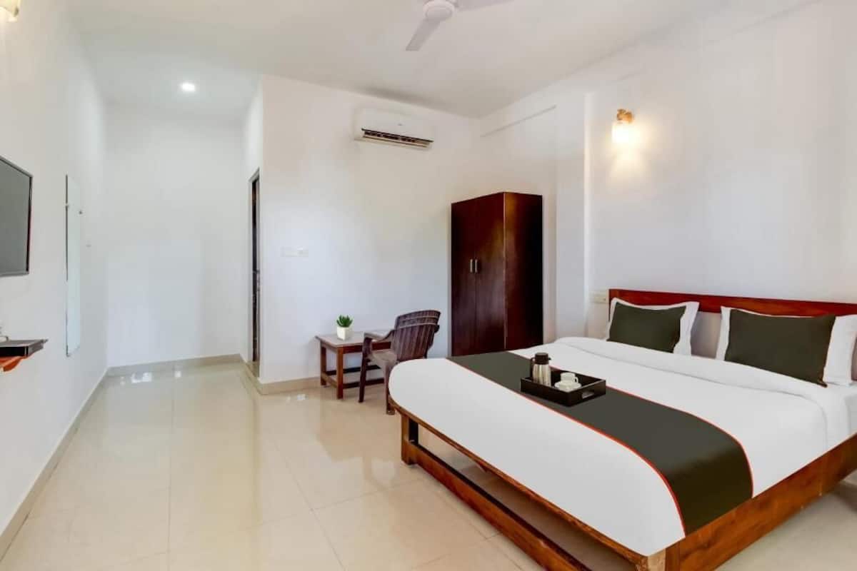 A hotel room with a large bed, a wardrobe, a desk with a chair, and a television on the wall.