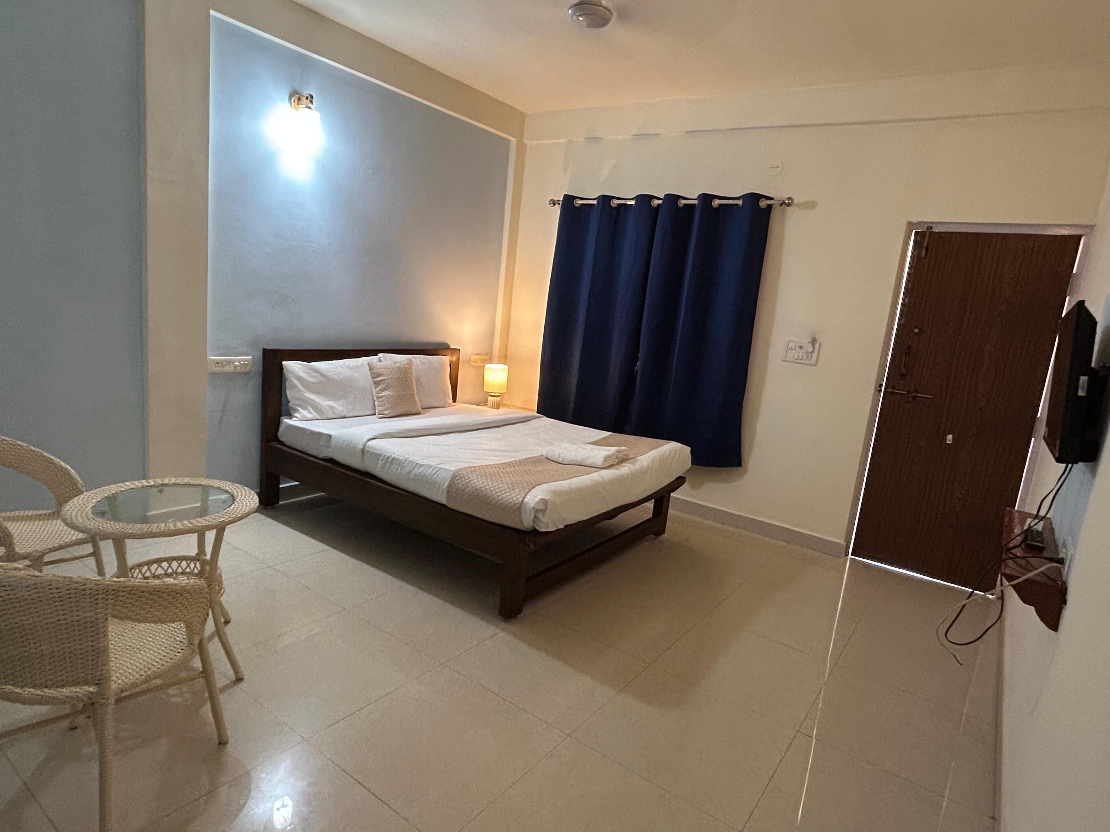 Una cama individual con ropa blanca, una mesita de noche, una lámpara, una silla y una puerta.