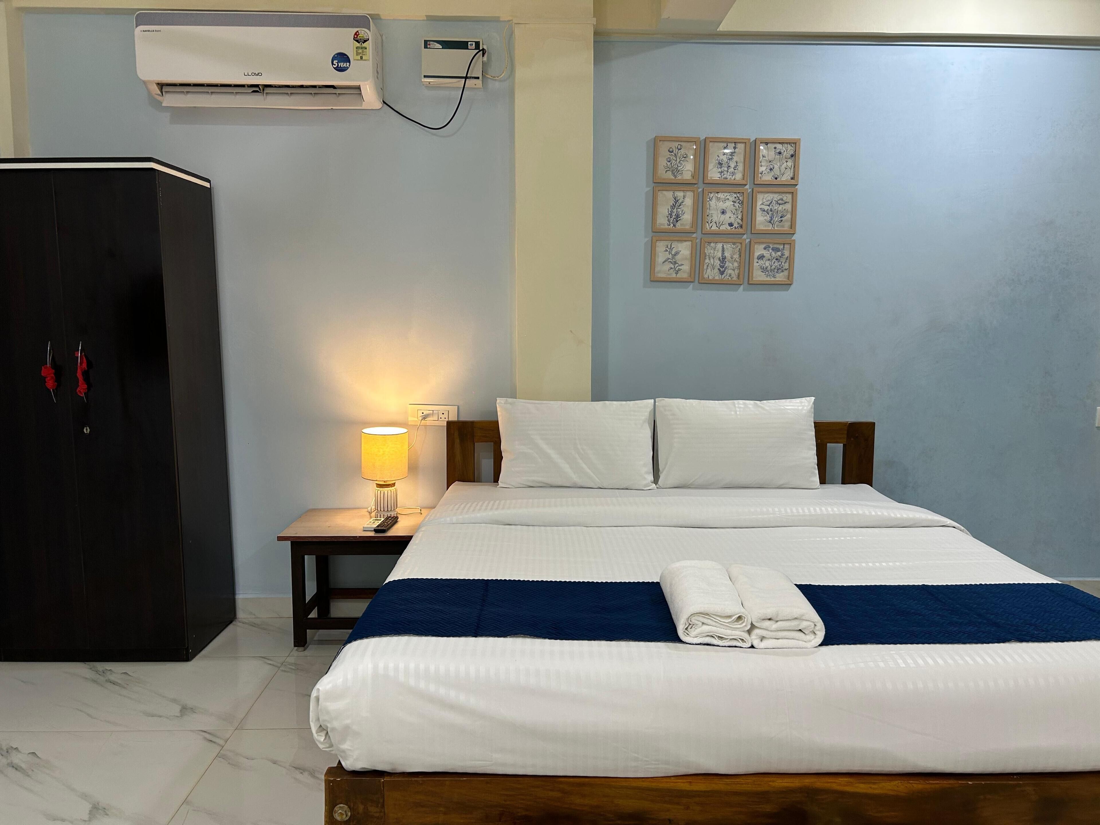 A hotel room with a bed, a nightstand with a lamp, a wardrobe, and a wall-mounted air conditioner.