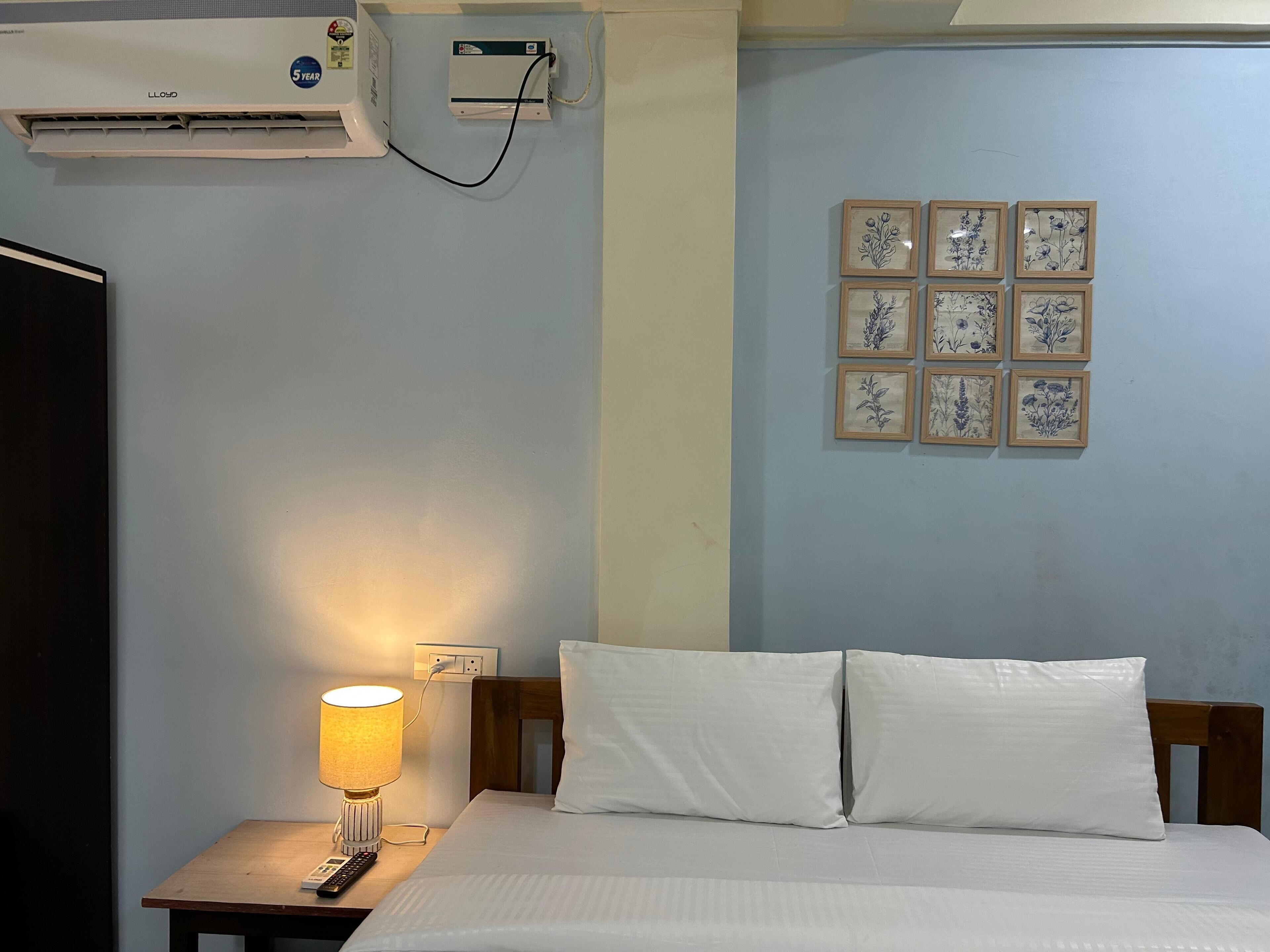 Habitación de hotel con cama, lámpara de noche, equipo de aire acondicionado y decoración floral en la pared.