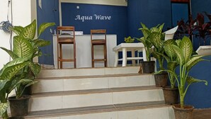 A reception area with a blue wall, two wooden chairs, a white table, and several potted plants. - Aqua Wave by YogiTree Hotels (Morjim)