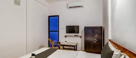 A hotel room with a bed, a desk, a chair, a TV, and a wardrobe.