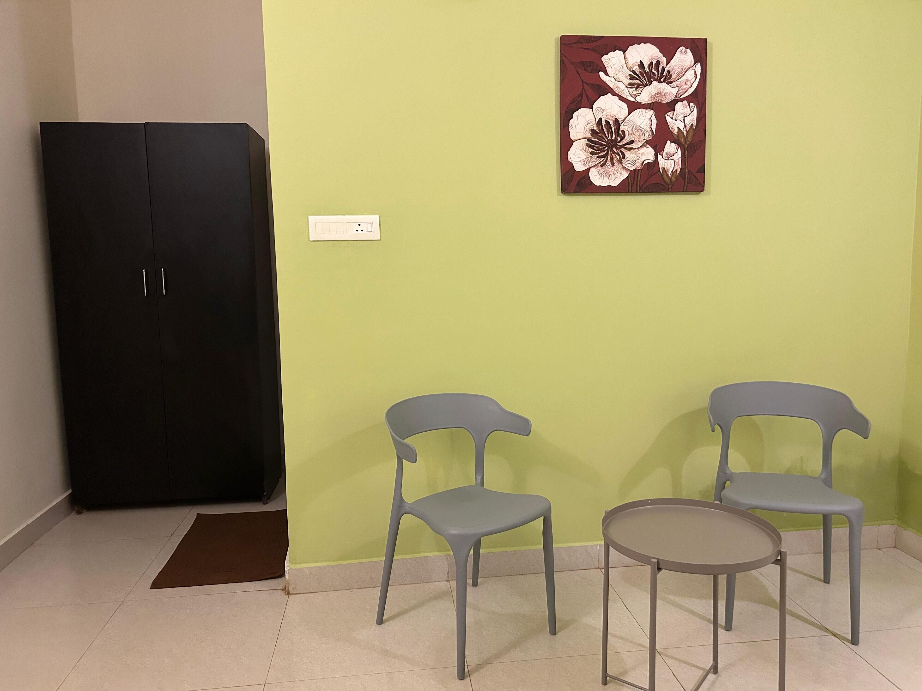Una habitación con dos sillas grises, una mesa redonda pequeña, un armario negro y una obra de arte floral en la pared.
