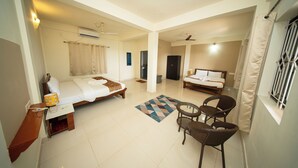 A hotel room with two beds, a sitting area with chairs, a small table, a rug, and a window with curtains. - Aqua Wave by YogiTree Hotels (Morjim)