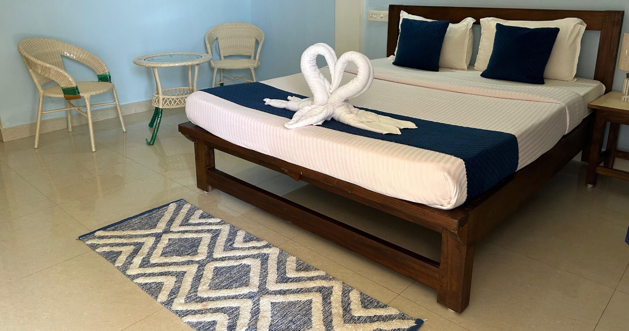 Una cama bien hecha con una colcha azul y blanca, un cabecero de madera y dos almohadas.