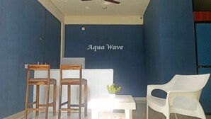 A room with a blue wall, two wooden chairs, a white table with a small plant, and a white chair. - Aqua Wave by YogiTree Hotels (Morjim)