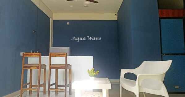 A room with a blue wall, two wooden chairs, a white table with a small plant, and a white chair. - Aqua Wave by YogiTree Hotels (Morjim)