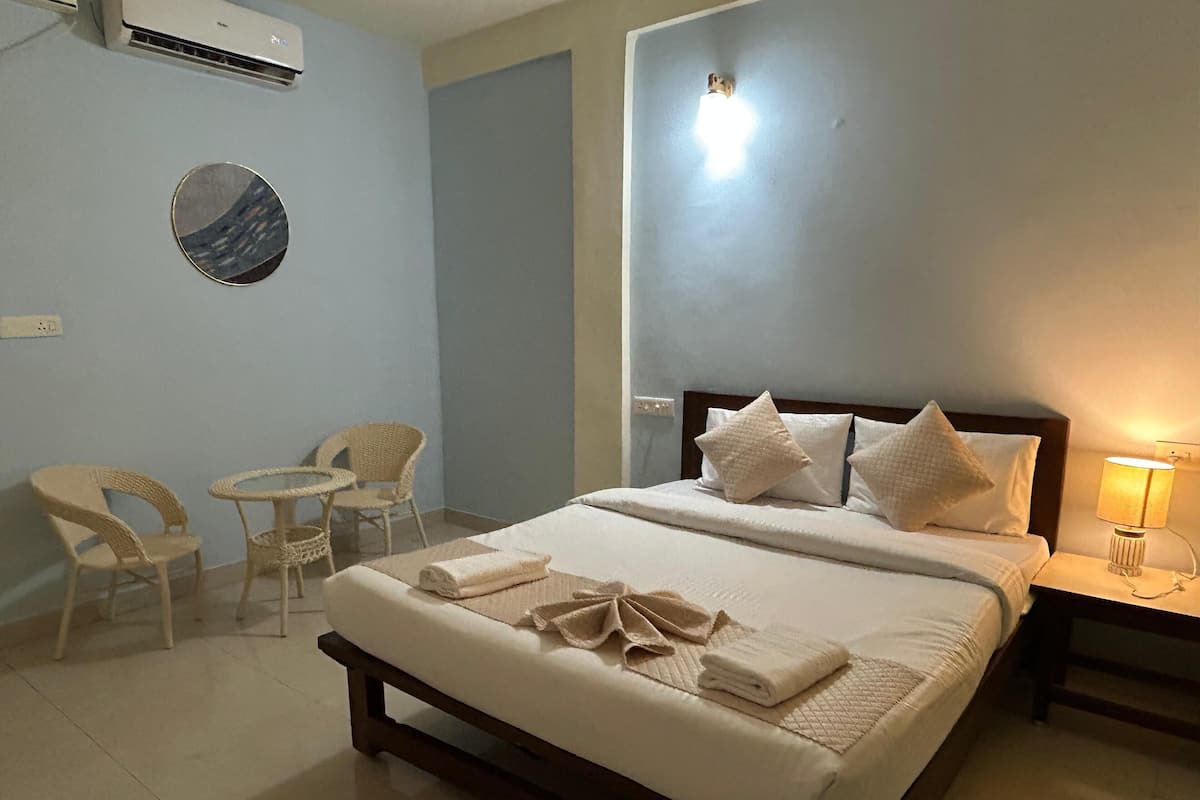 A neatly arranged hotel room with a bed, bedside table, lamp, two chairs, and a round mirror.