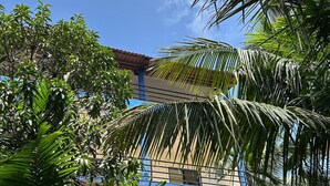 A building with a red-tiled roof and a blue facade, surrounded by lush green foliage. - Aqua Wave by YogiTree Hotels (Morjim)