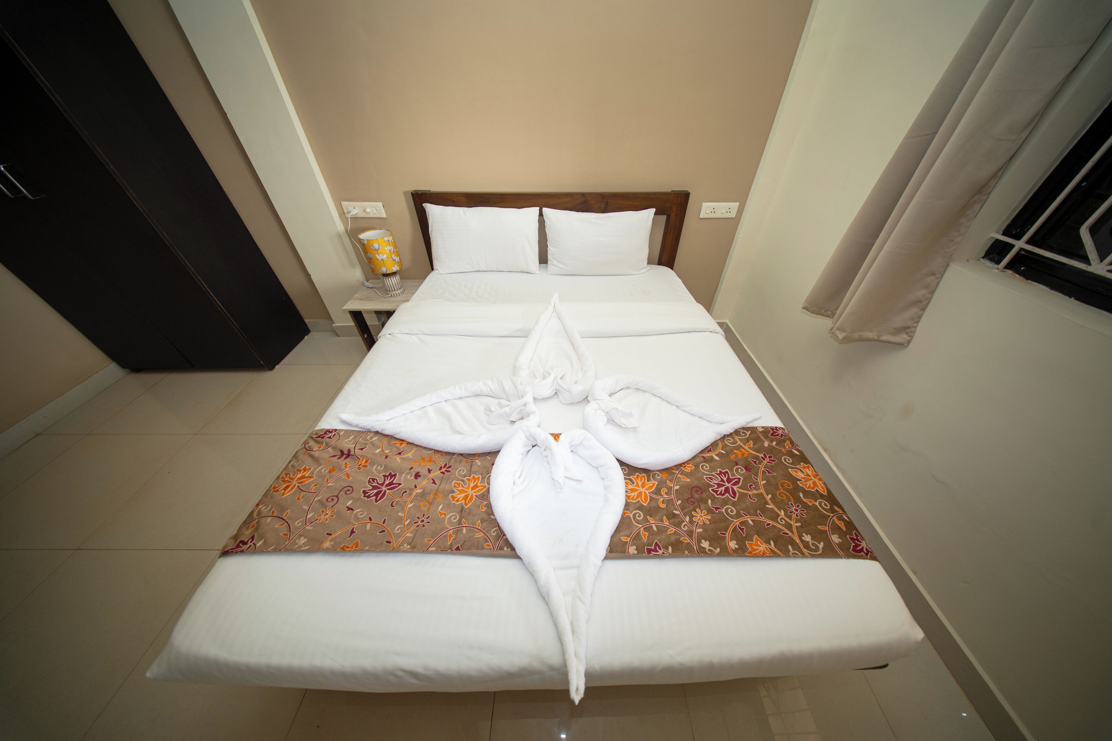 A neatly made bed with a decorative towel arrangement, a wooden headboard, and a patterned bedspread.