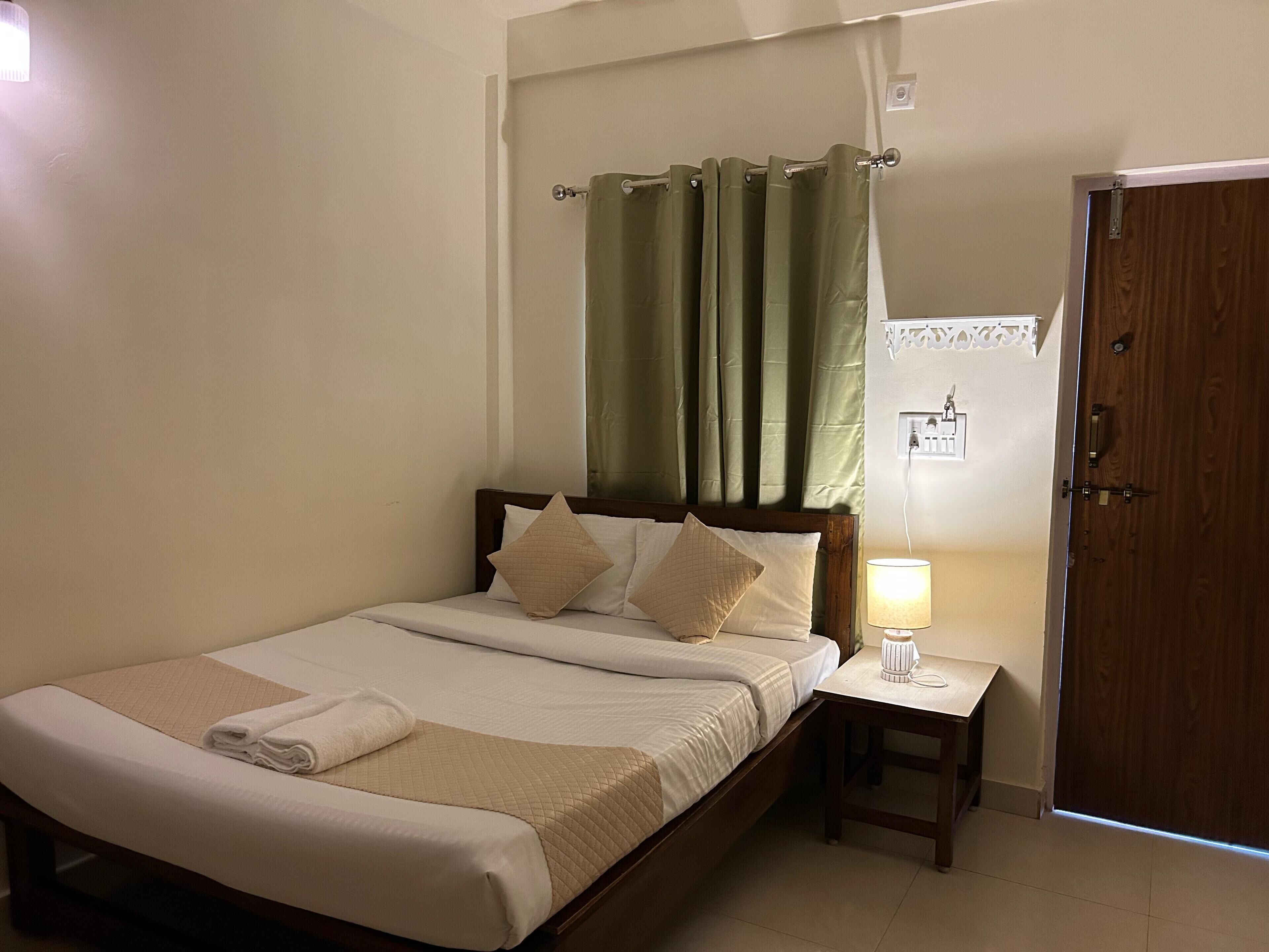 A neatly made bed with a quilted blanket, a bedside lamp, and a wooden door in a hotel room.