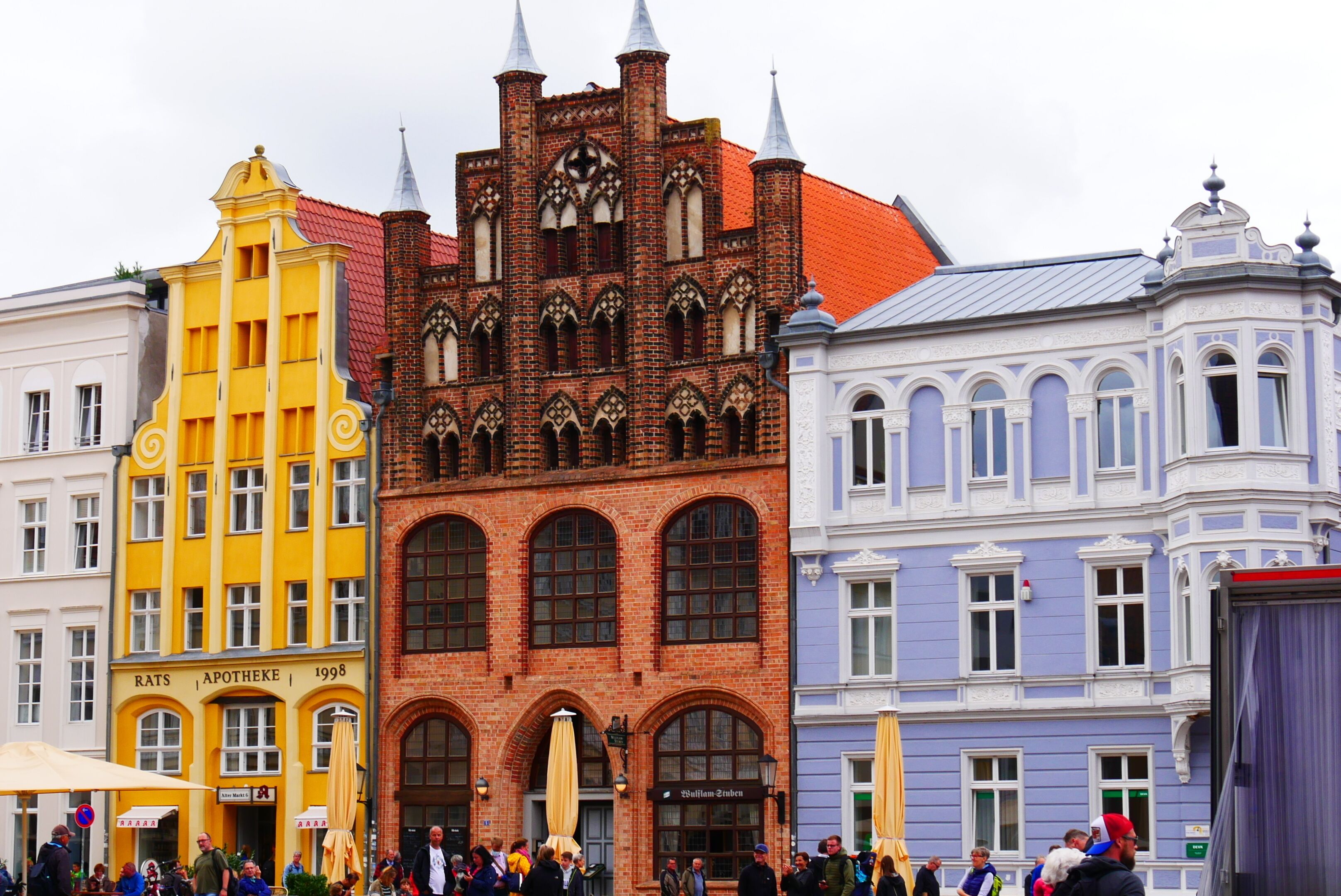 Un bâtiment historique à la façade en briques et aux fenêtres en arc de cercle, entouré d’immeubles aux couleurs vives.