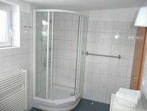 Une salle de bain moderne avec une douche à parois de verre, des murs recouverts de carreaux blancs, un porte-serviettes et un radiateur apparent.