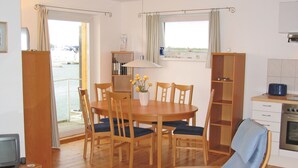 A dining area with a wooden table and chairs, a small kitchen with a stove, and a view through the windows. - Floating Houses - Komfortable Schwimmende Ferienhäuser im Krösliner Yachthafen (Kröslin)