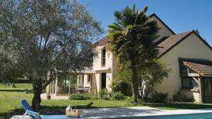 Un espace aménagé au bord de la piscine, avec des chaises longues, une piscine et une maison dotée d’un jardin.