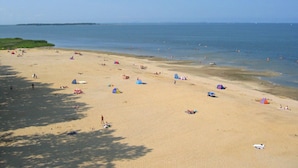 Une vaste plage de sable fin, parsemée de tentes et de parasols, avec une eau calme et un ciel dégagé.