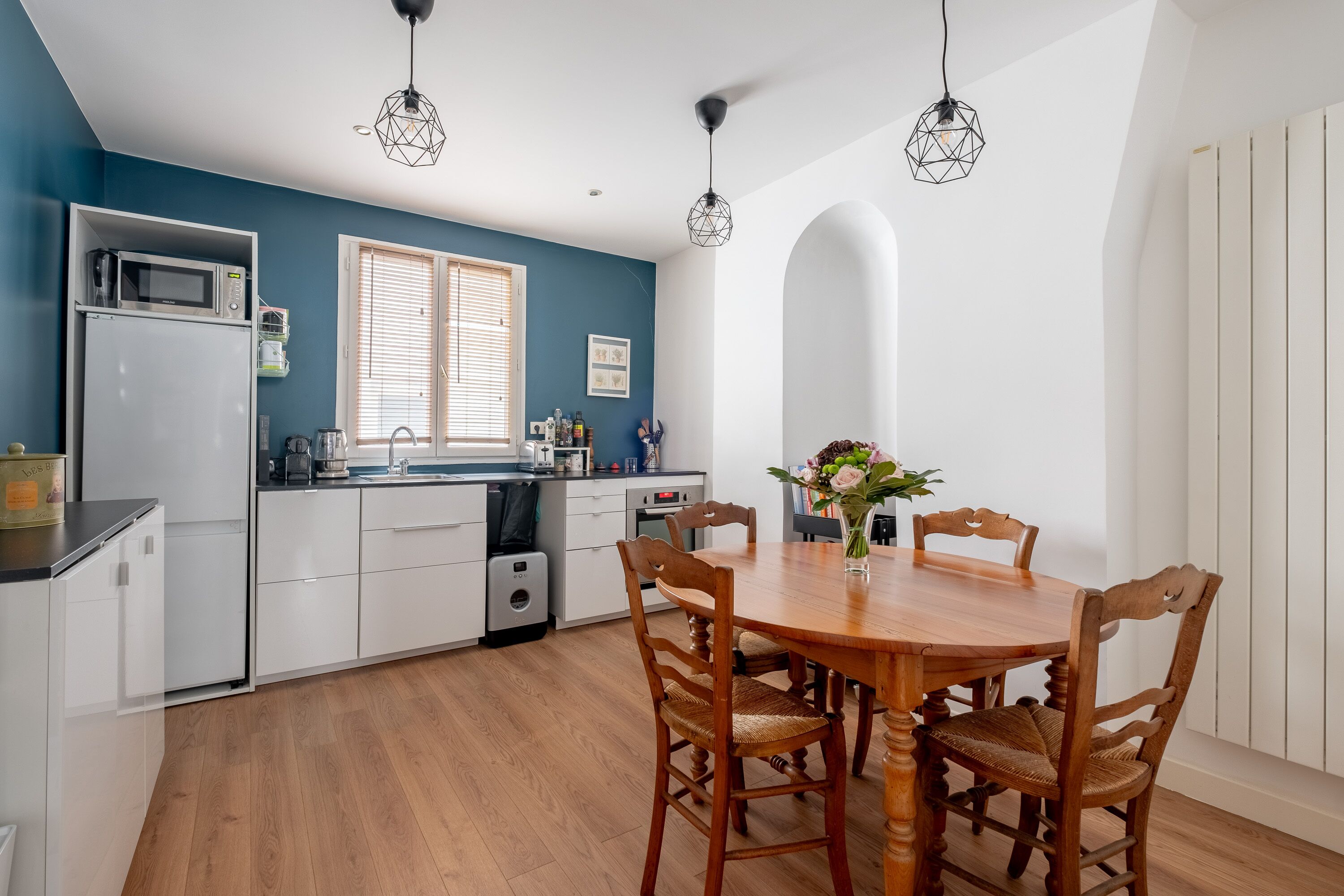 A modern kitchen with white cabinets, a microwave, and a sink. There is a dining table with chairs and a vase of flowers.