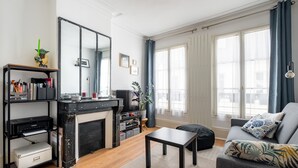 Una sala de estar con chimenea, un sofá con cojines estampados, una mesita de centro y una estantería con diversos objetos.