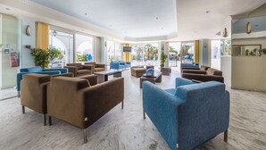 A spacious lobby with multiple seating areas, large windows, and a pool view. - Laganas Holidays Hotel (Zakynthos)