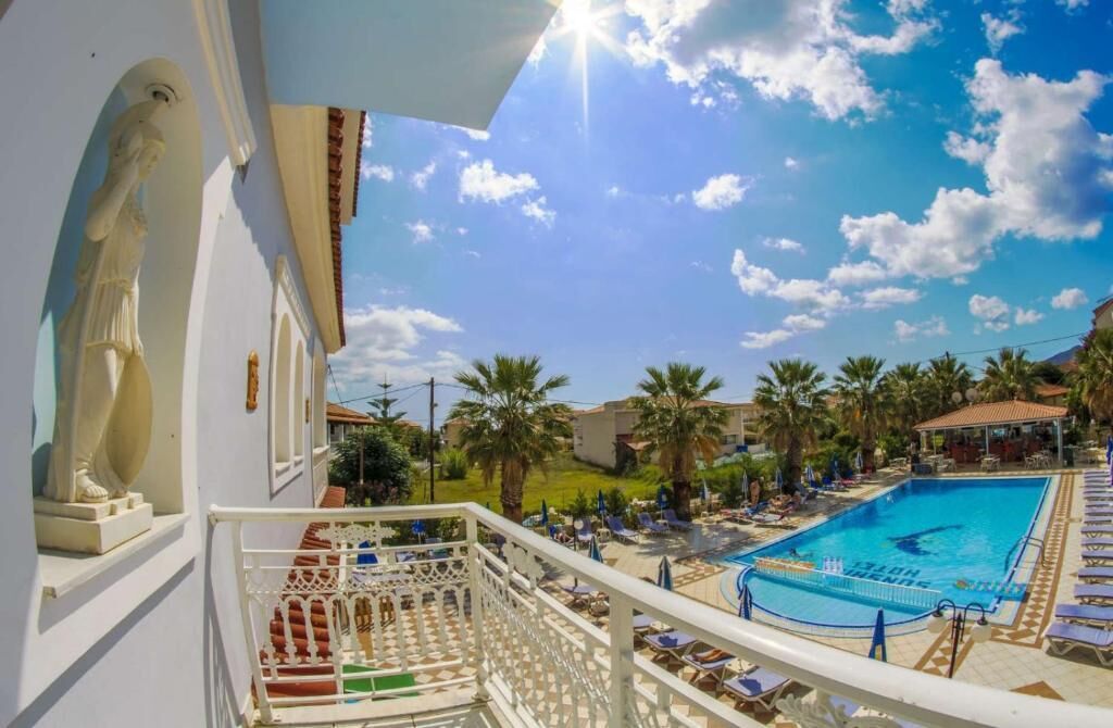 Zona de piscina con sillones de descanso, cielo despejado y un edificio con una estatua.