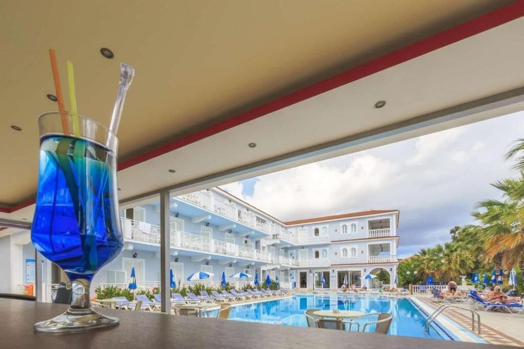 A poolside view with a clear sky, a glass with a straw, and a building with balconies.
