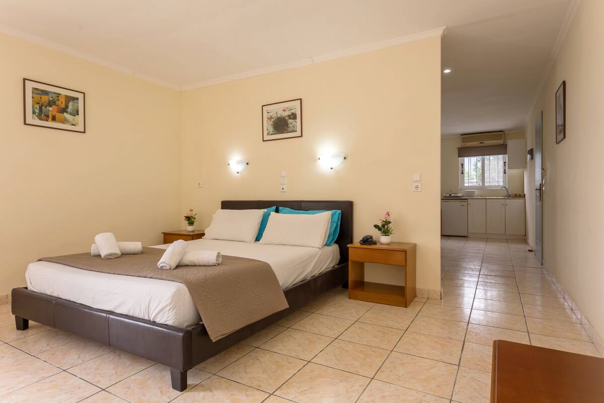 Quarto com cama, mesas de cabeceira e vista para a cozinha.