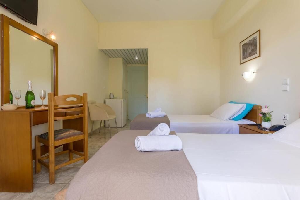 Habitación de hotel con escritorio, dos camas, una silla, un espejo y una mesita con una botella y vasos.