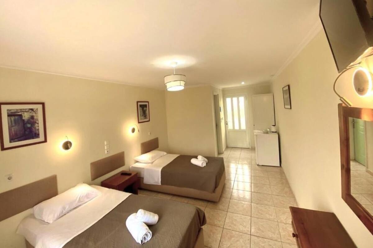 Quarto de hotel com duas camas, uma escrivaninha, um espelho e uma pequena cozinha.