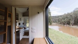 A compact room with a wooden bench, a small kitchenette, and a view of a river. - Tiny Thomas Summary: (Upper Colo)