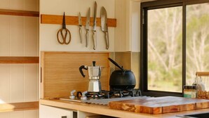 A kitchen with wooden cabinets, a stove, a coffee maker, and a window with a view of trees. - Tiny Thomas Summary: (Upper Colo)