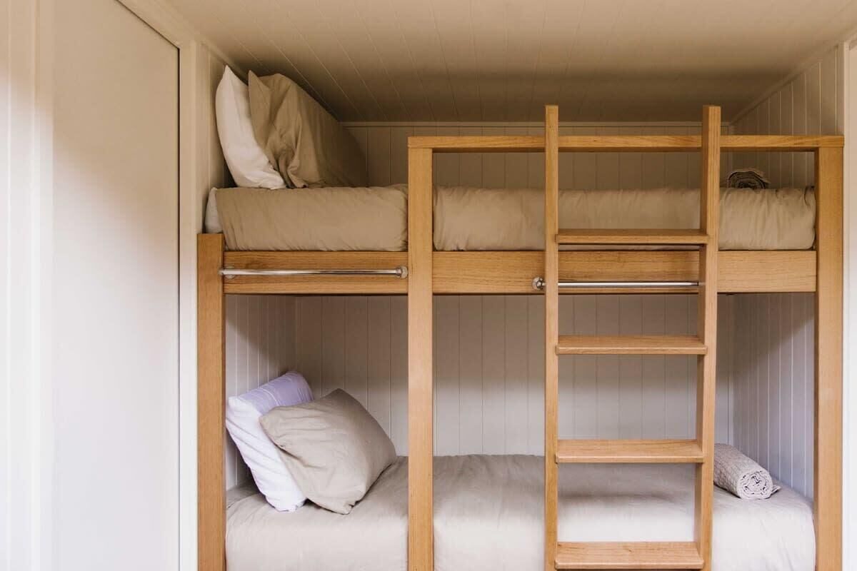A bunk bed with a ladder, a lower bed with pillows, and a rolled towel.