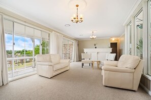 A spacious living room with large windows, a chandelier, and a white fireplace. - Large Kelso Family Home - Flexible Bedding (Kelso)