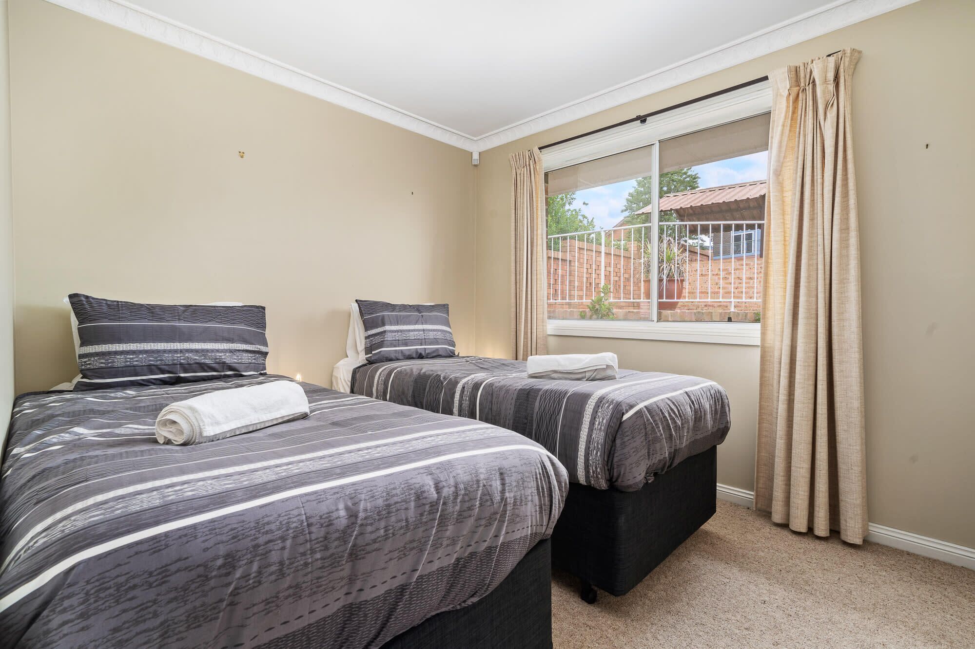 A bedroom with two beds, a window with curtains, and a view of a brick building outside.